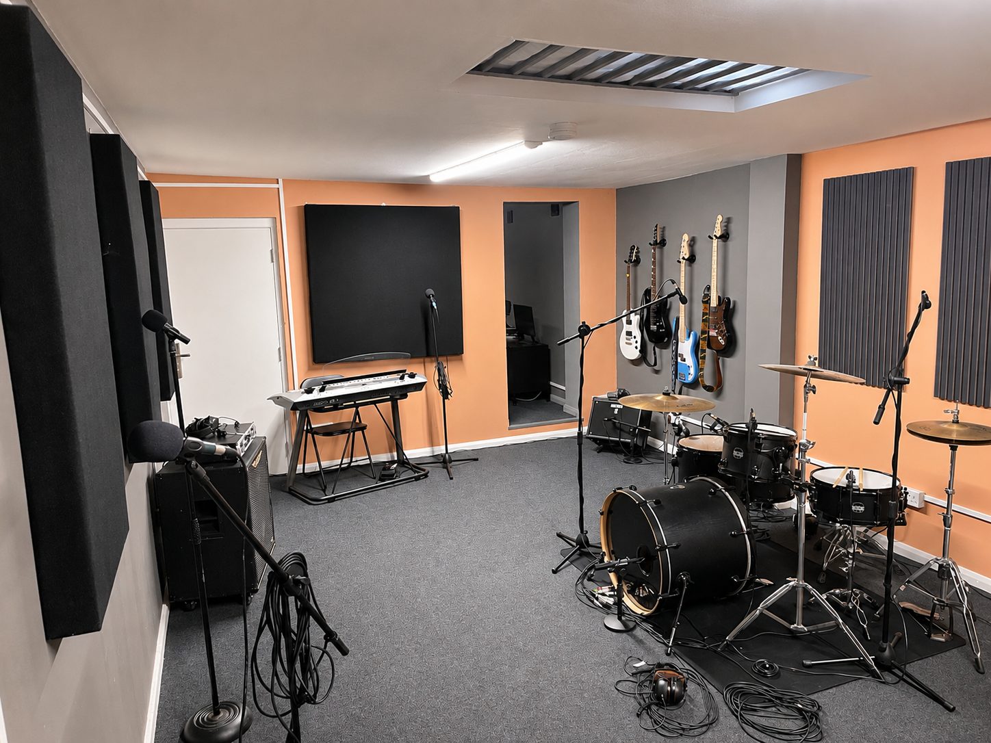 Live room with stage piano, wall-mounted guitars and drum kit